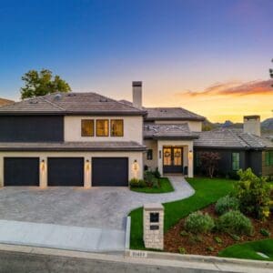 Modern two-story house with a three-car garage and a beautifully landscaped yard, nestled within the serene community of Sunset Trails, with a perfect view of the sunset in the background.