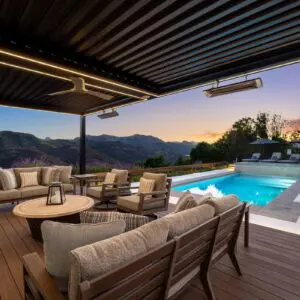 The outdoor patio with seating overlooks a dazzling pool and the majestic Sunset Trails, offering a breathtaking mountain view at dusk.