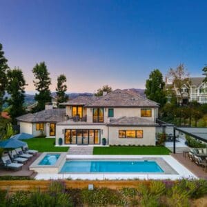 A large two-story house on Sunset Trails features a backyard pool, patio, and lush greenery, all set against the serene backdrop of hills at dusk.