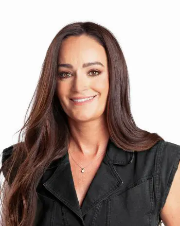 Meet Your Team: A woman with long dark hair wearing a sleeveless black denim jacket smiles at the camera against a plain white background.