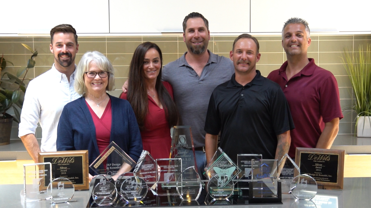 A group of six people stand together smiling, with various awards and plaques displayed on a table in front of them.