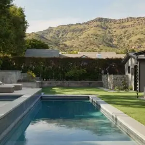 A rustic North Ranch backyard features a rectangular swimming pool, lounge chairs on a concrete deck, a grassy area, and a charming house. Mountains are visible in the background.