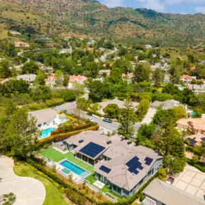 Aerial view of the rustic North Ranch suburban neighborhood with houses, swimming pools, and green landscapes, surrounded by hills. Several roofs are equipped with solar panels.