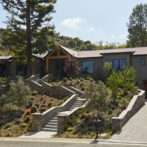 A modern hillside home in Rustic North Ranch with large windows, multiple trees, and a well-maintained garden. Stone steps and a paved driveway lead to the house.