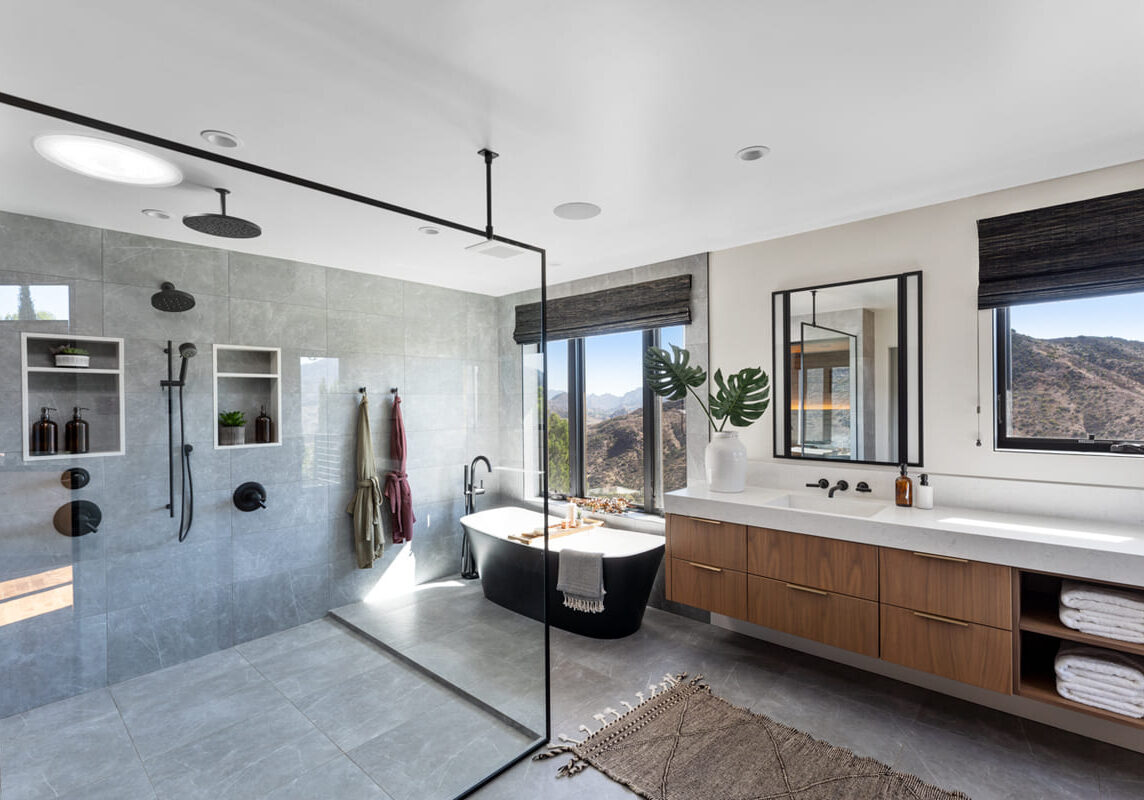 Modern bathroom featuring a spacious walk-in shower, a freestanding bathtub, and a large mirror above a wooden vanity. Large windows offer mountain views, creating the perfect modern refreshment retreat.